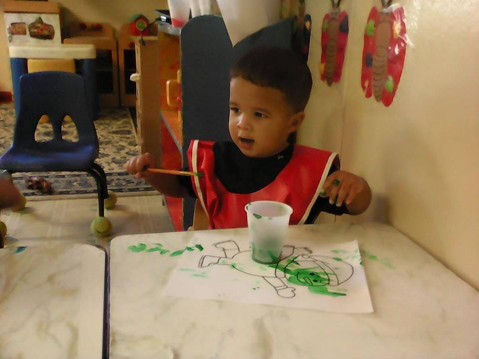 Child in a red smock painting with green paint at a table