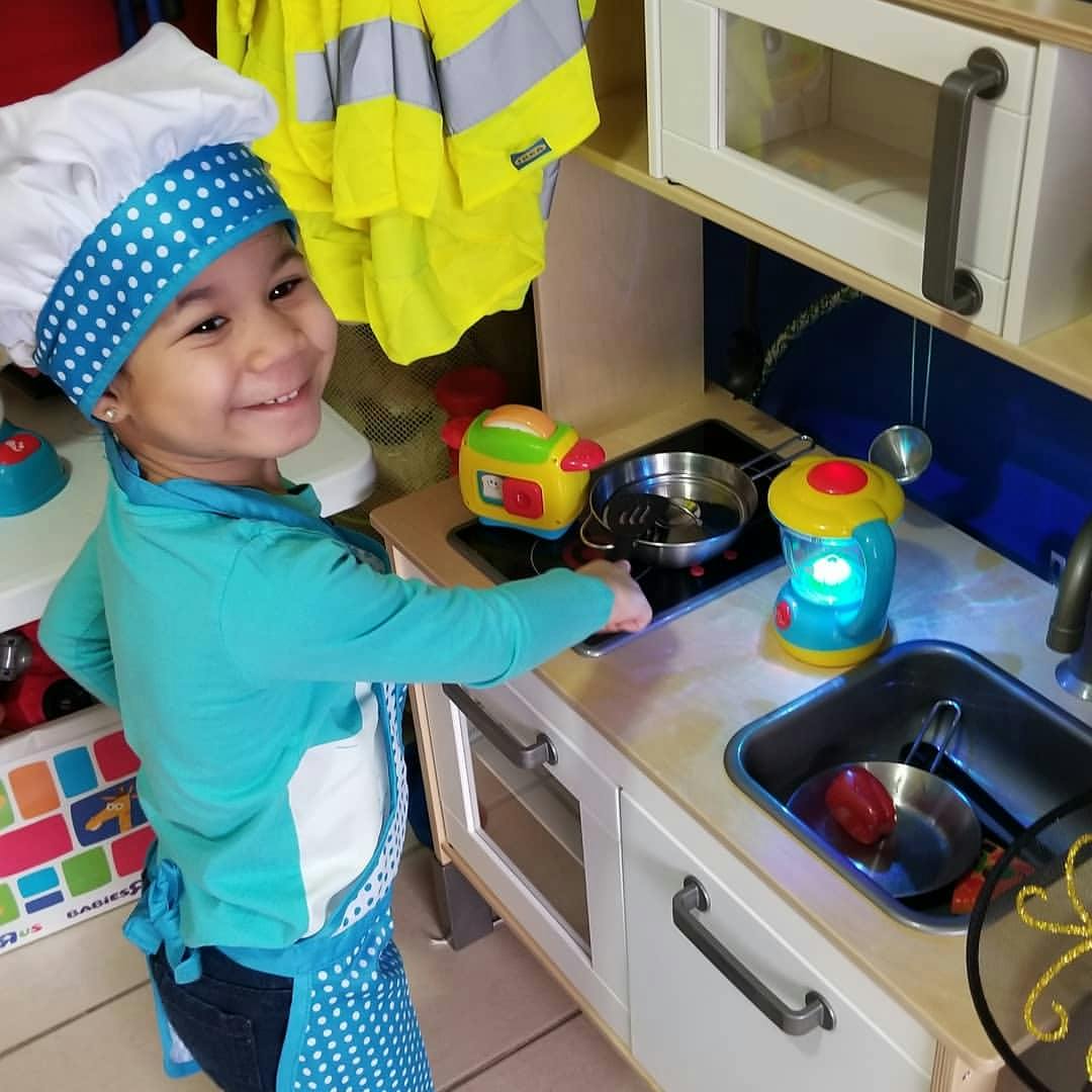 Child in a chef hat and apron playing in a toy kitchen