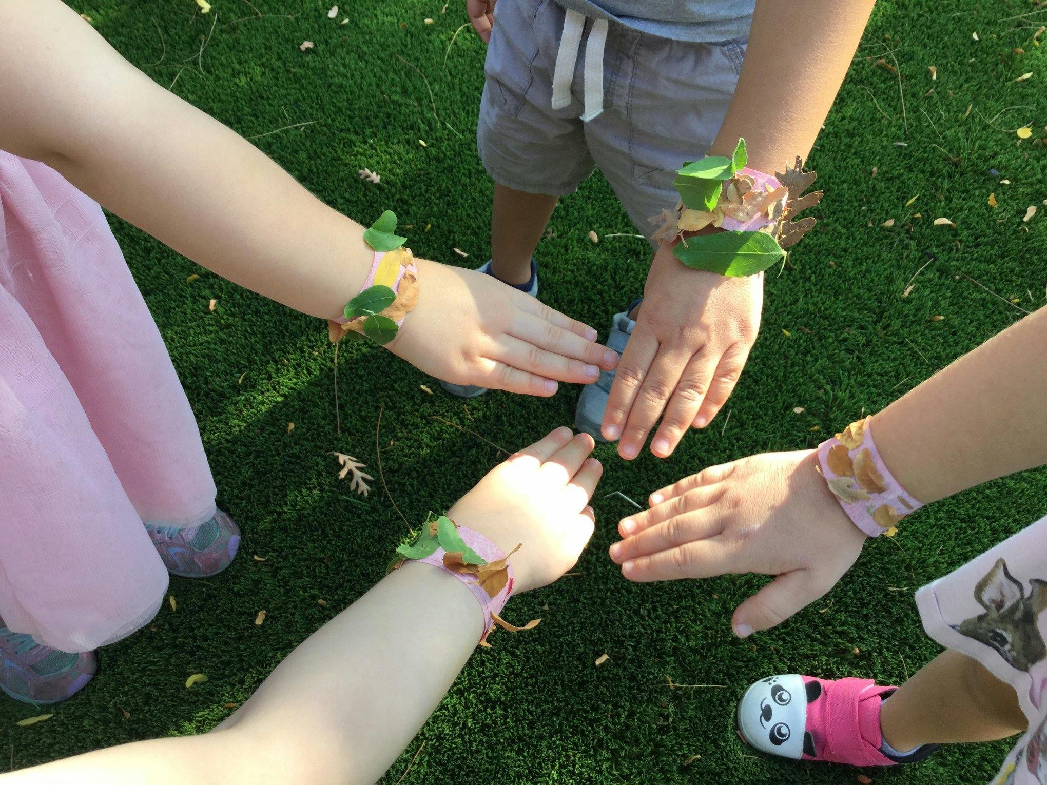 Children's hands with leaf and flower bracelets touching in a circle
