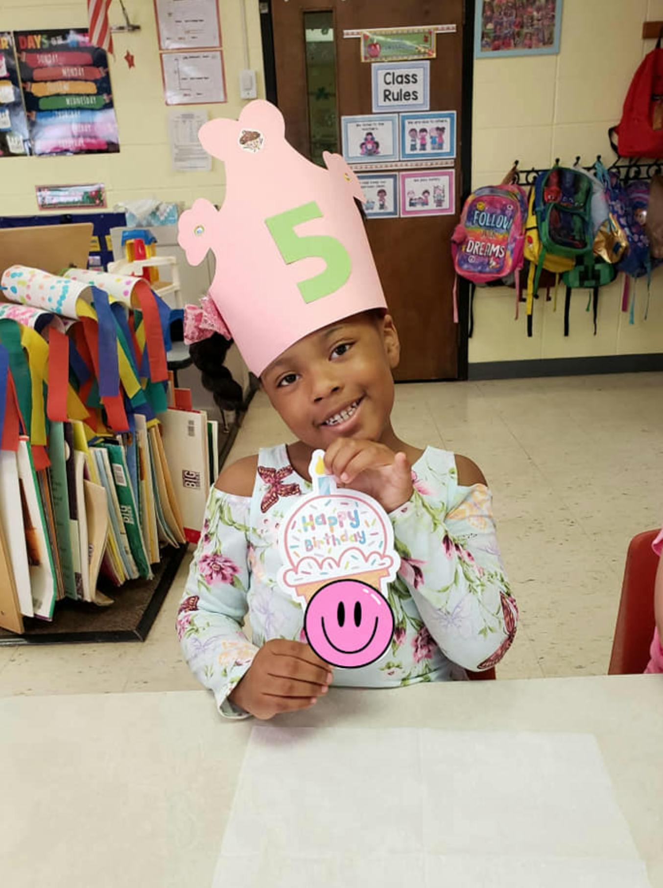 Child wearing a pink birthday crown with a number 5, holding a happy birthday sign