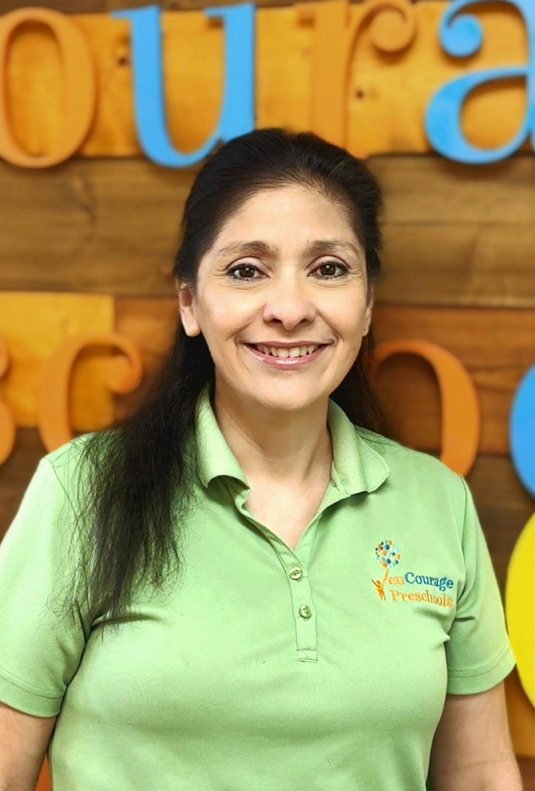 Smiling person in a green polo shirt with the logo "Courage Preschool"