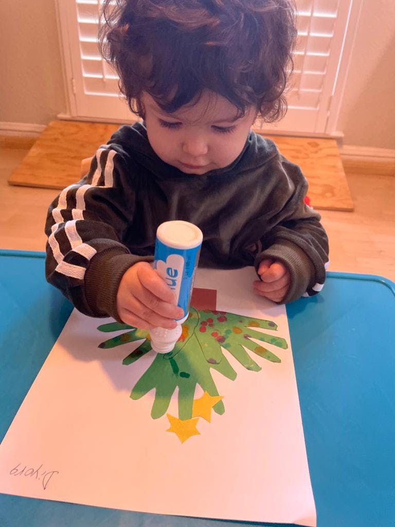 Child decorating a paper Christmas tree with a glue stick