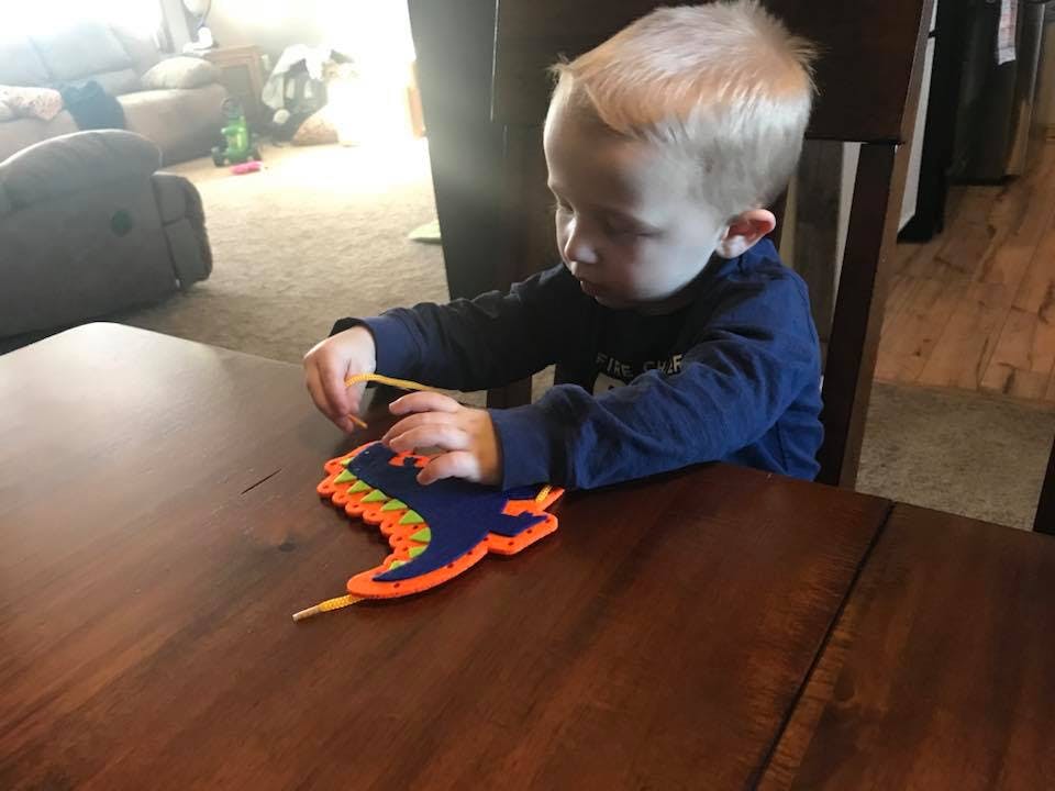 Child playing with a colorful lacing toy at a table