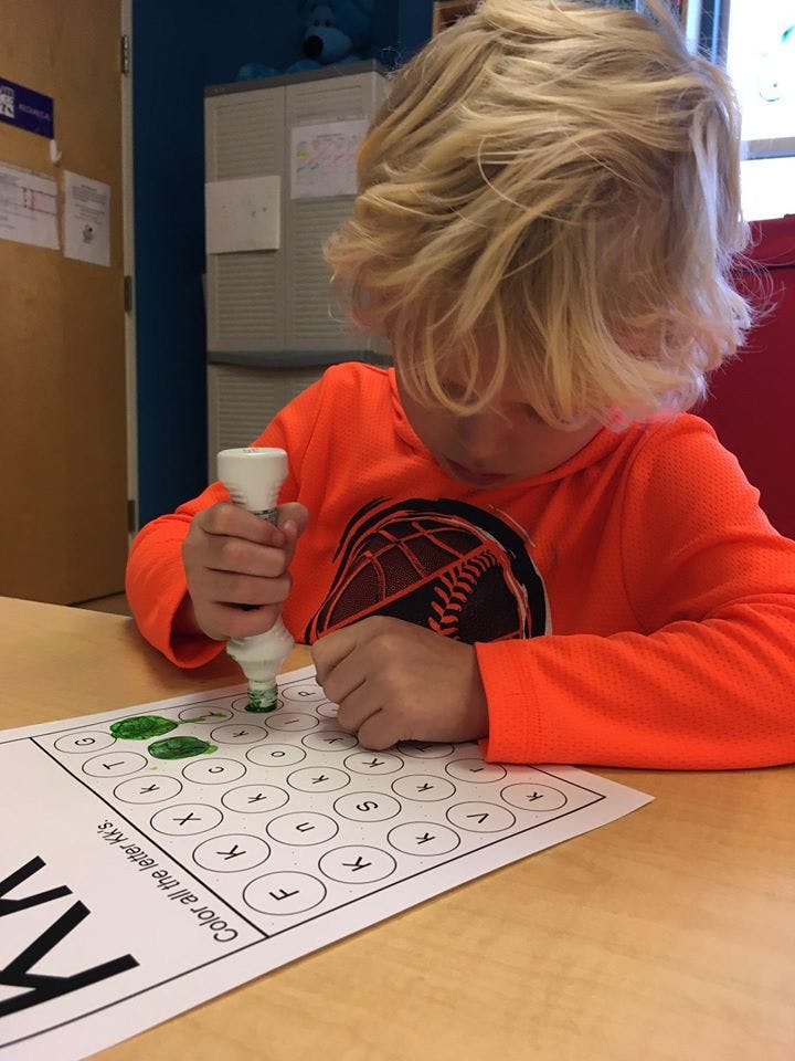 Child using a green dot marker on a paper with letters