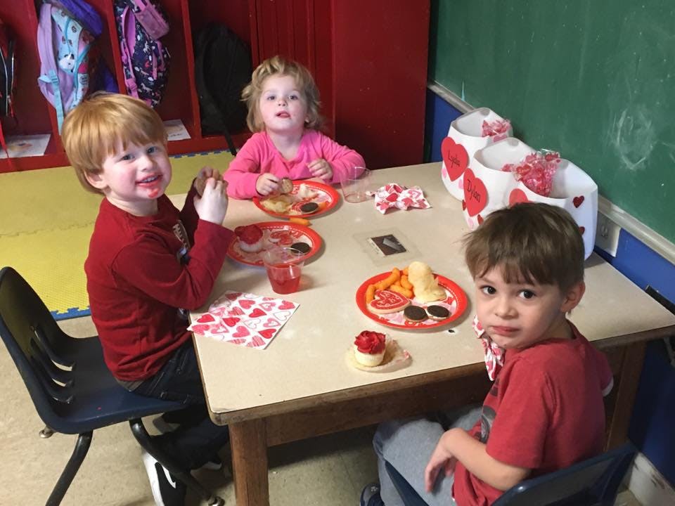 Three children sitting at a table with plates of food