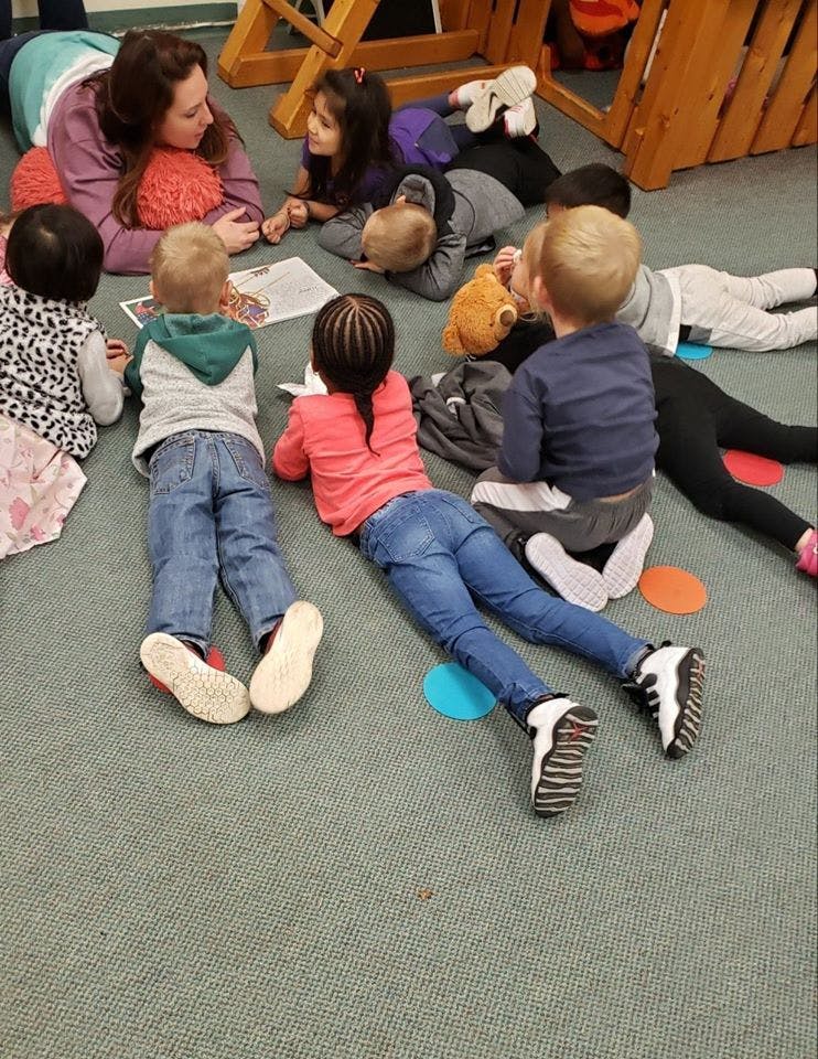 Adult and multiple children lying on floor looking at paper