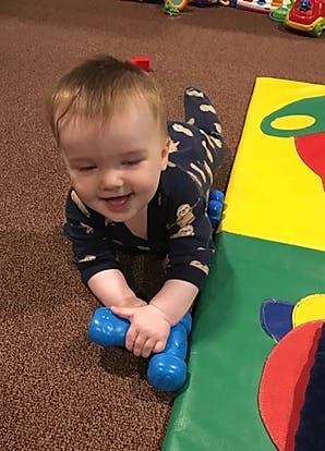 Child crawling on floor holding a blue toy