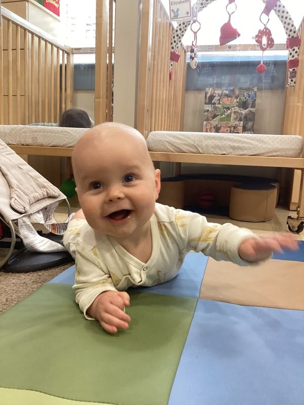 A baby lying on a mat in a nursery reaching forward