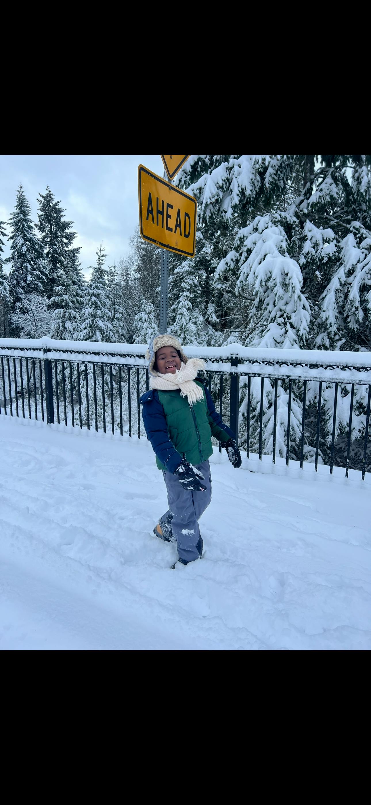 Child in winter clothing standing in snow with an "AHEAD" sign