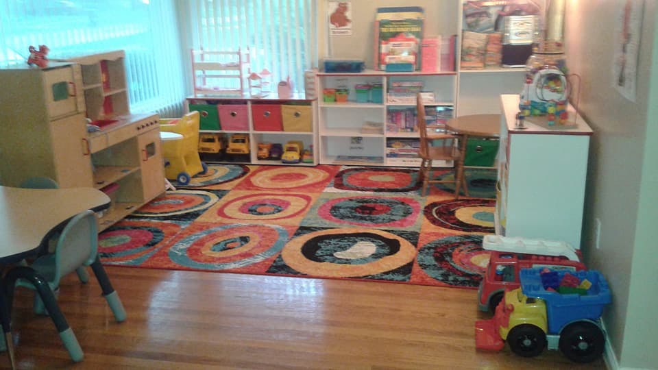Playroom with colorful rug, shelves of toys, and small table and chairs
