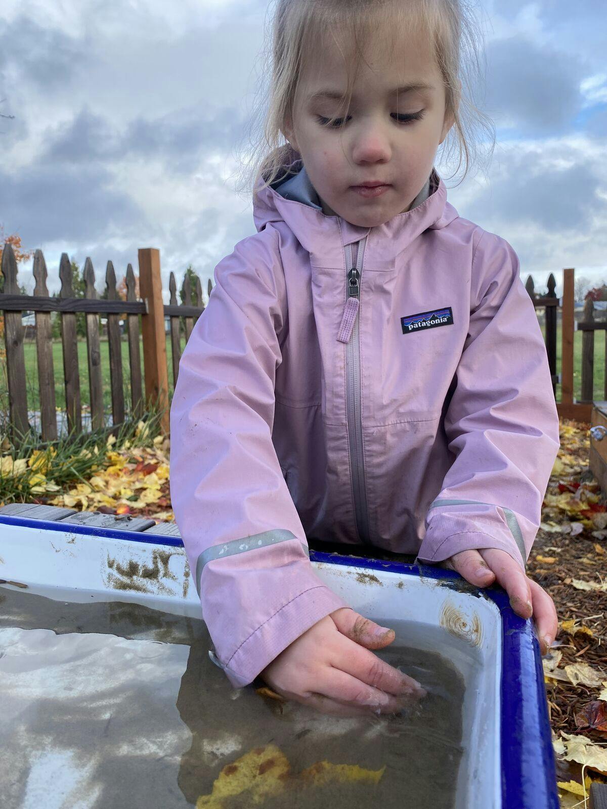 Child in a pink jacket playing in a water table