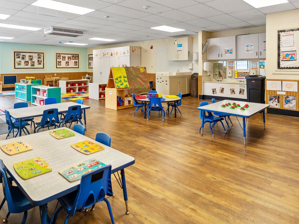 Empty colorful preschool classroom with tables, chairs, and learning stations