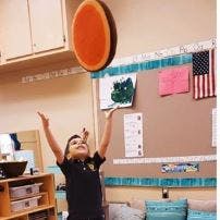 Child reaching for a large orange disc in a classroom