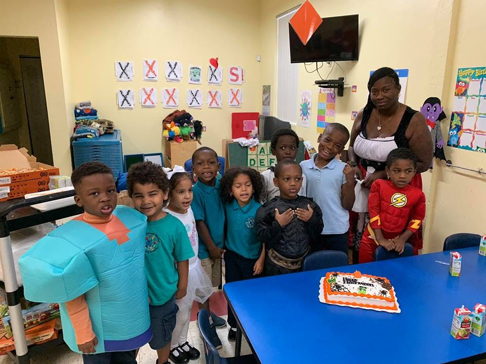 Adult and children posing for a photo in a classroom with a cake on a table