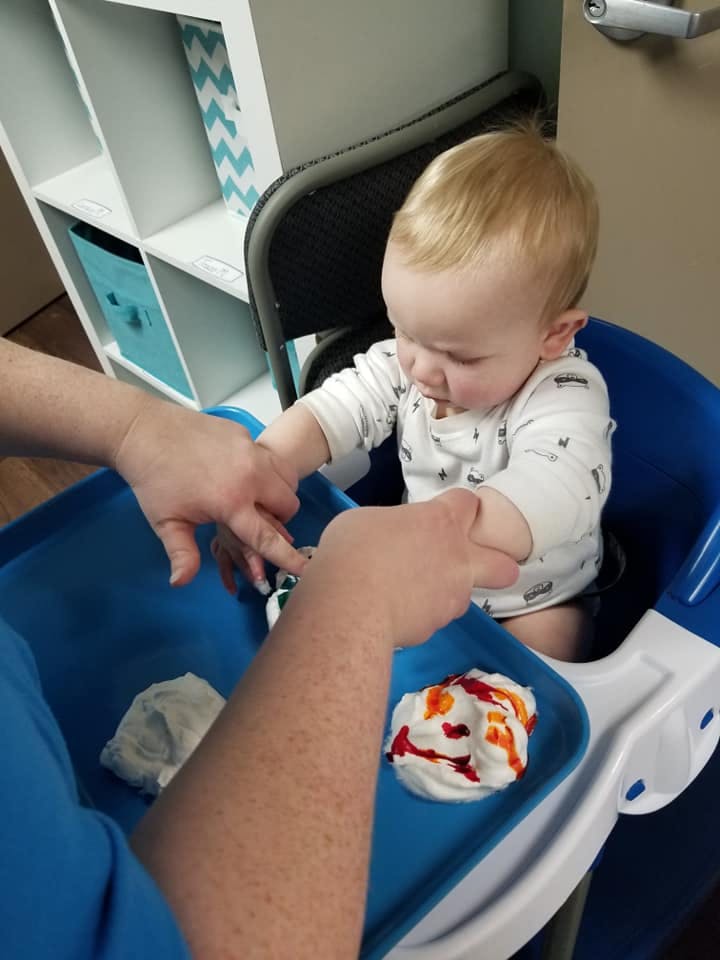 Adult helping a child in a high chair play with colorful shaving cream