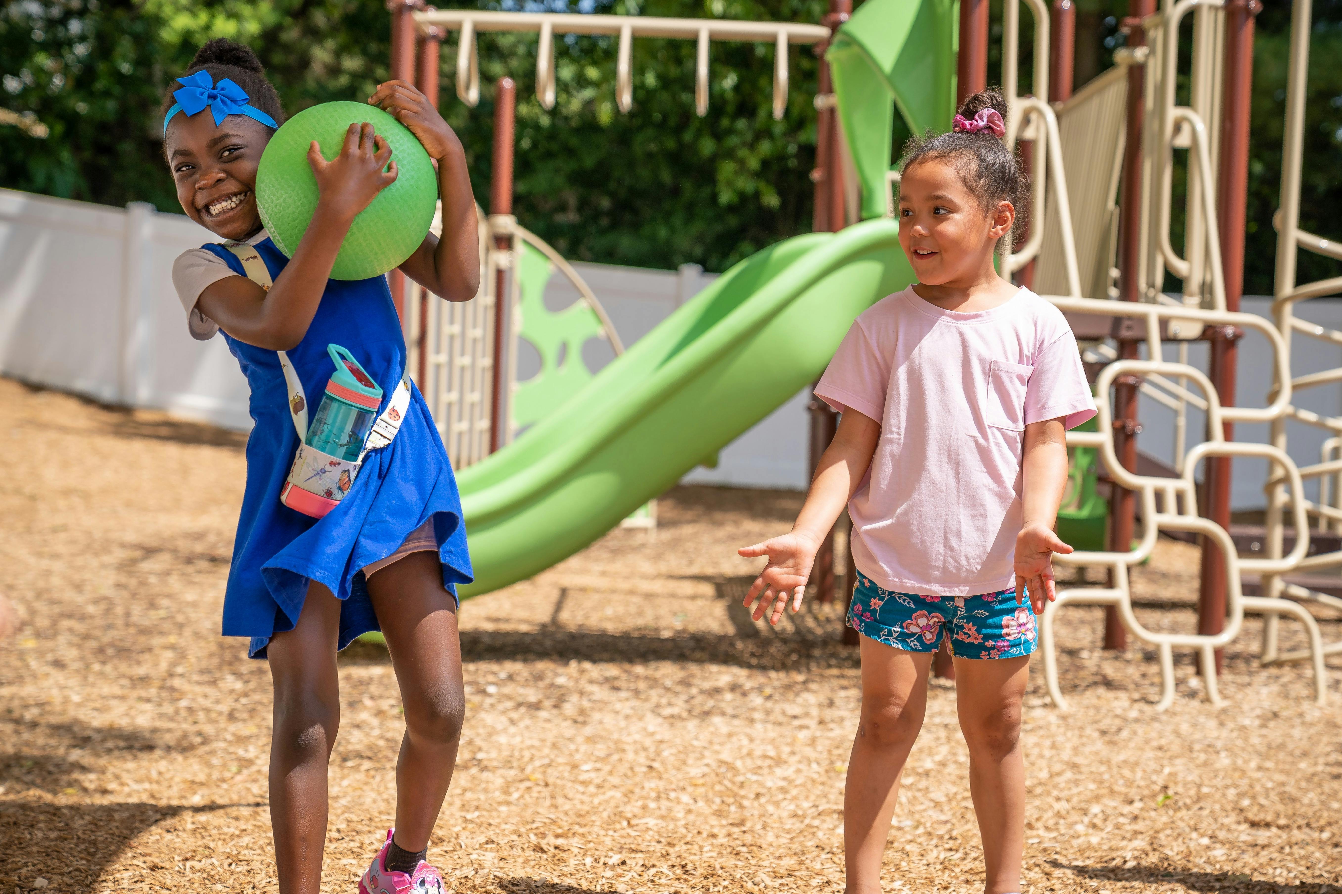 Two children playing with a green ball on a playground