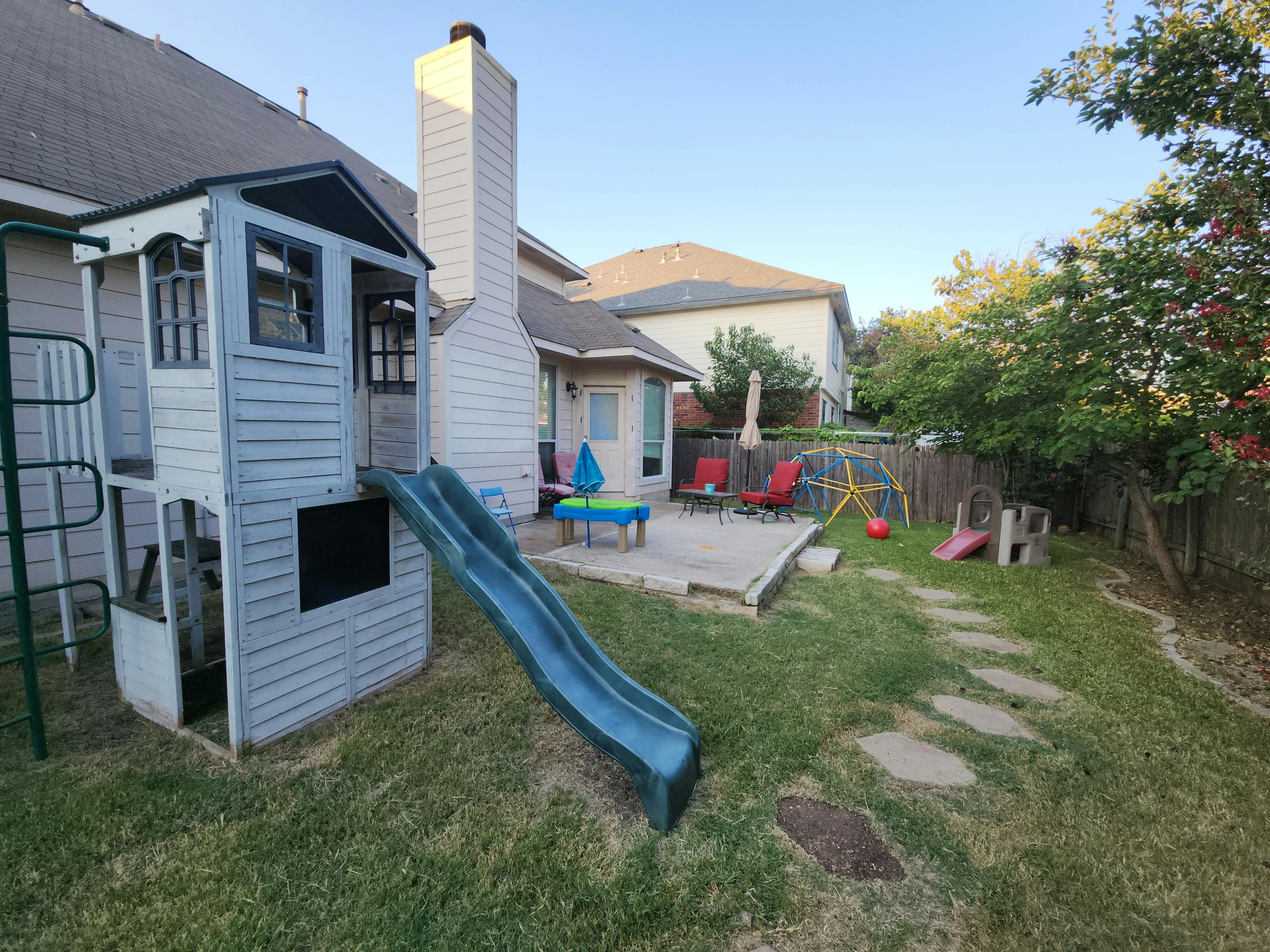 Backyard with a playhouse and slide, patio furniture, and stepping stones