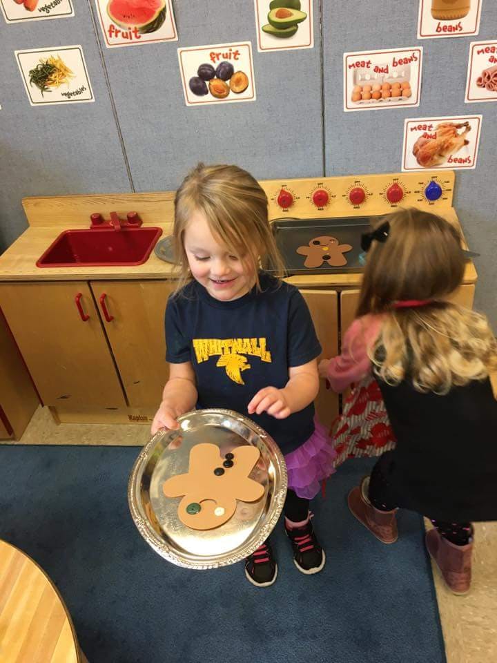 Child holding a tray with a gingerbread cutout in a play kitchen