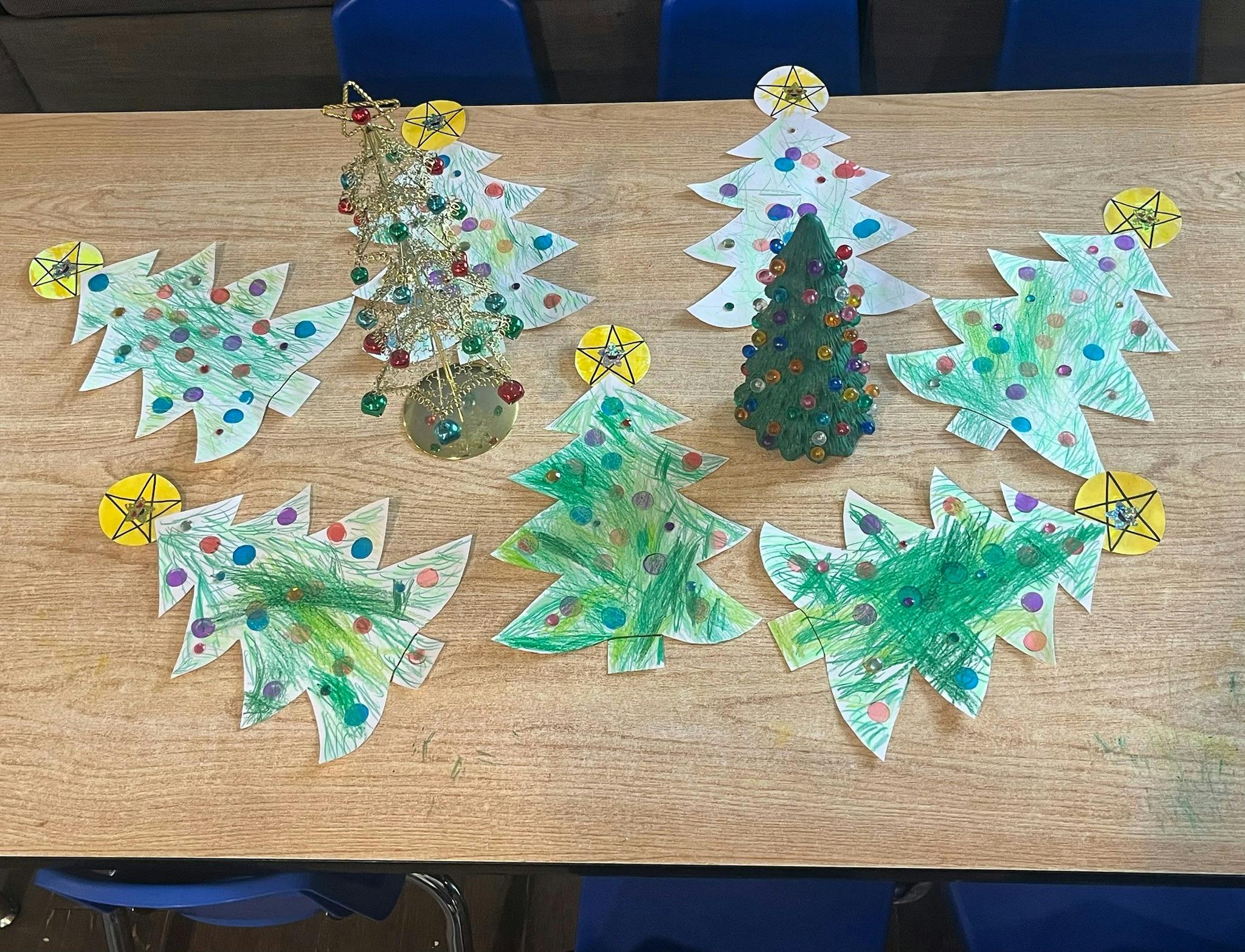 Paper cutout Christmas tree crafts on a table with two small decorative trees