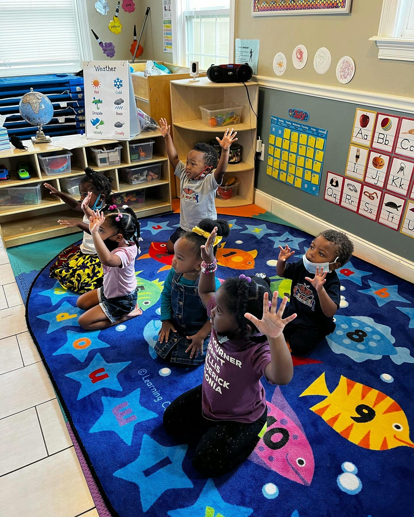 Children sitting on a rug with their hands raised