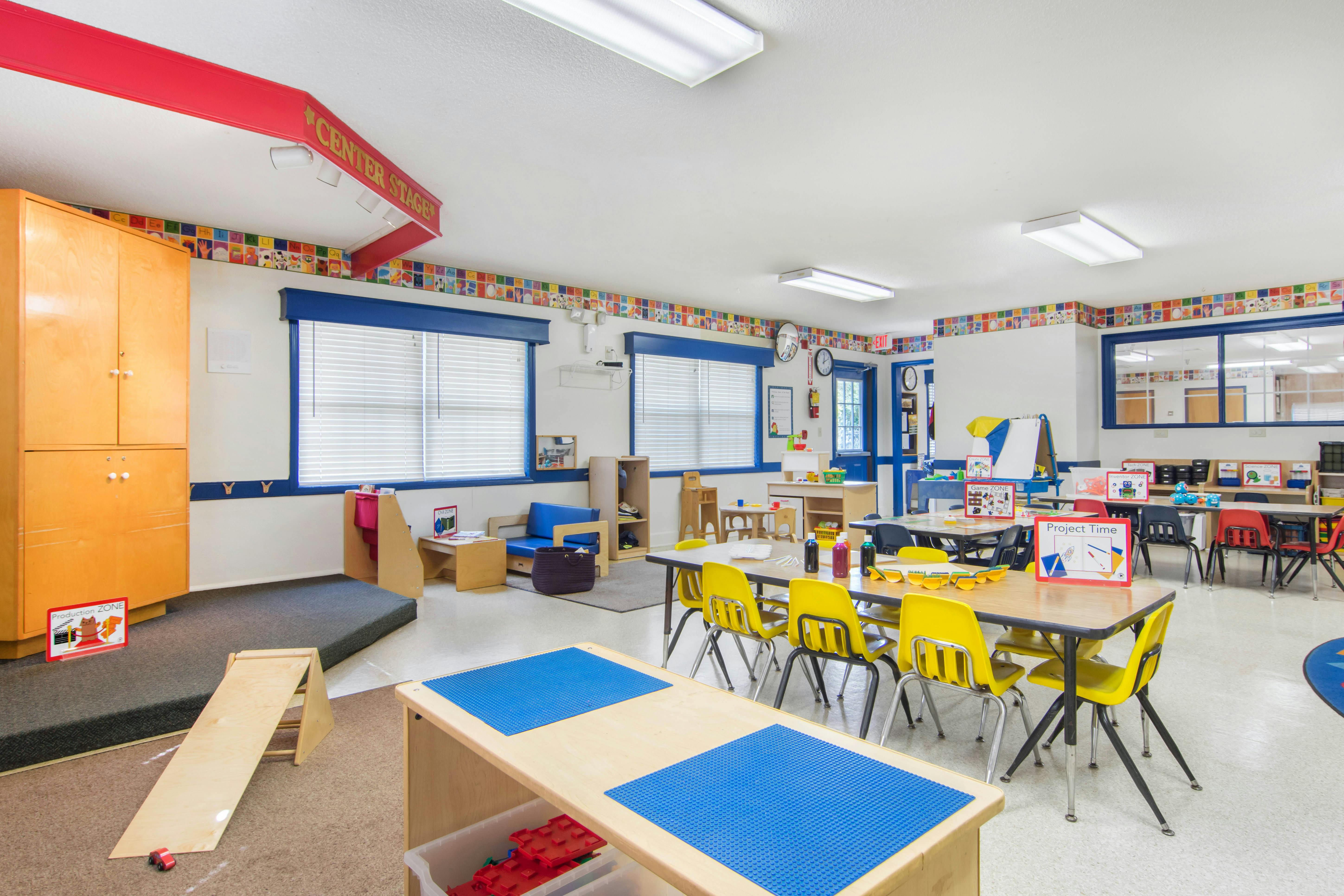 Empty classroom with small tables and chairs, play areas, and alphabet border