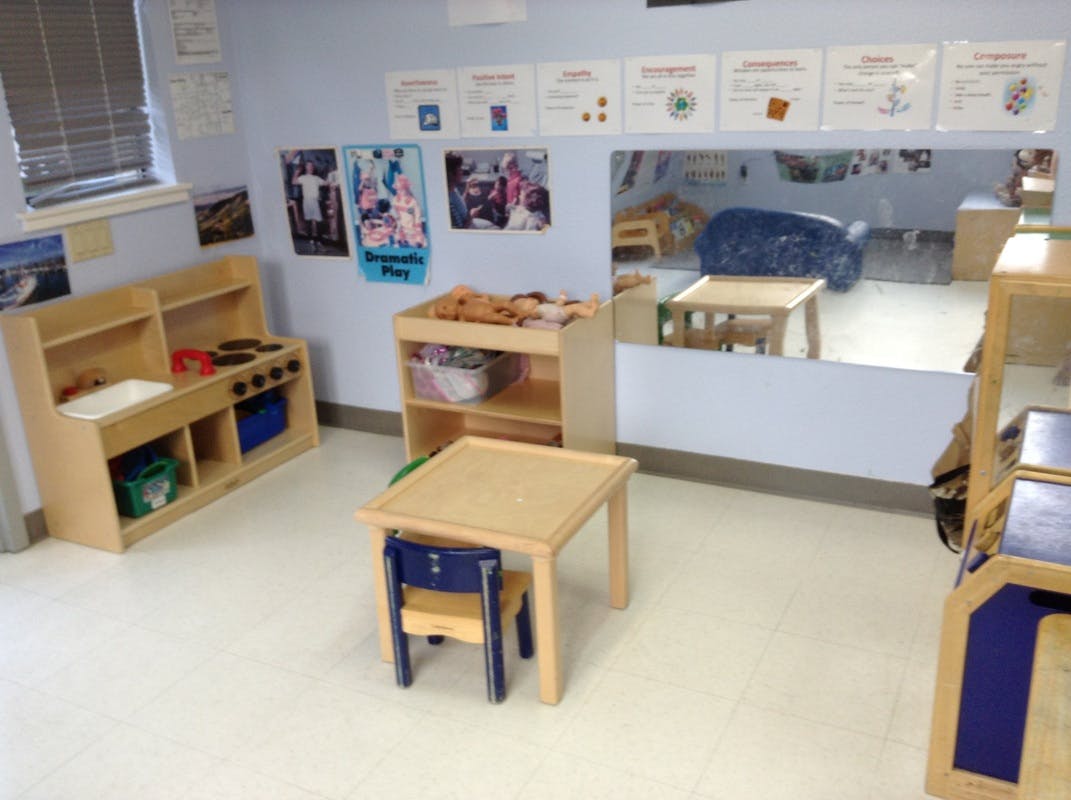 Classroom with small wooden tables and chairs, play kitchen, and mirror