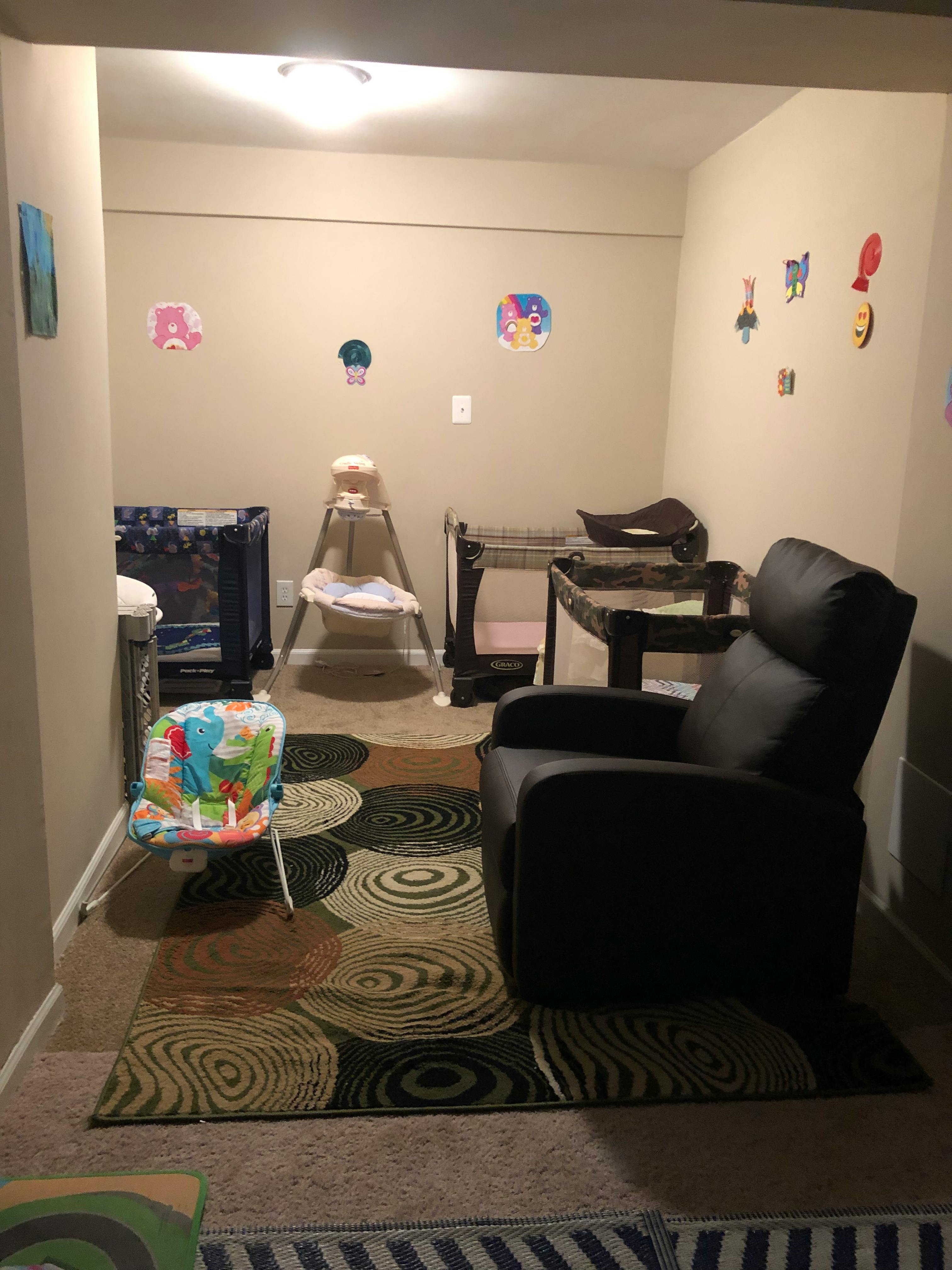Room with baby playards, high chair, and recliner