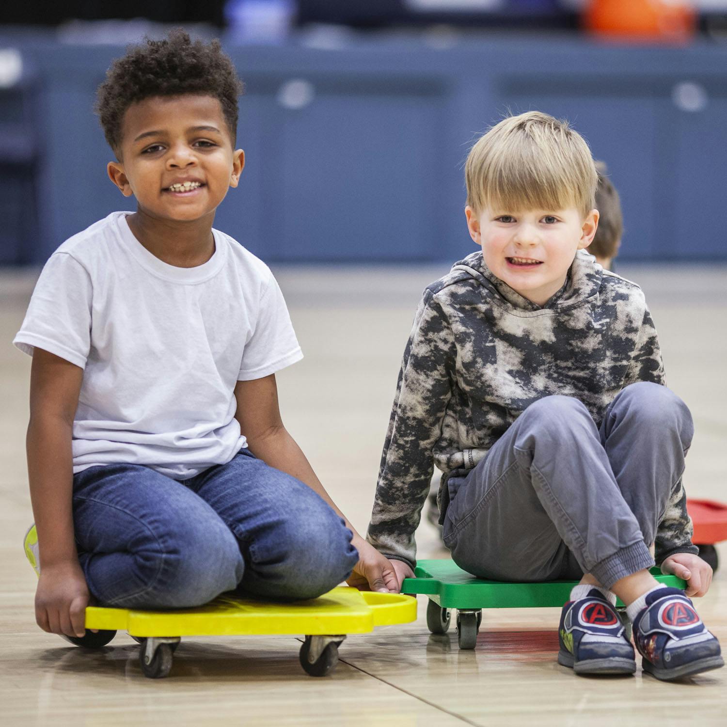 Two children sitting on scooter boards in a gym