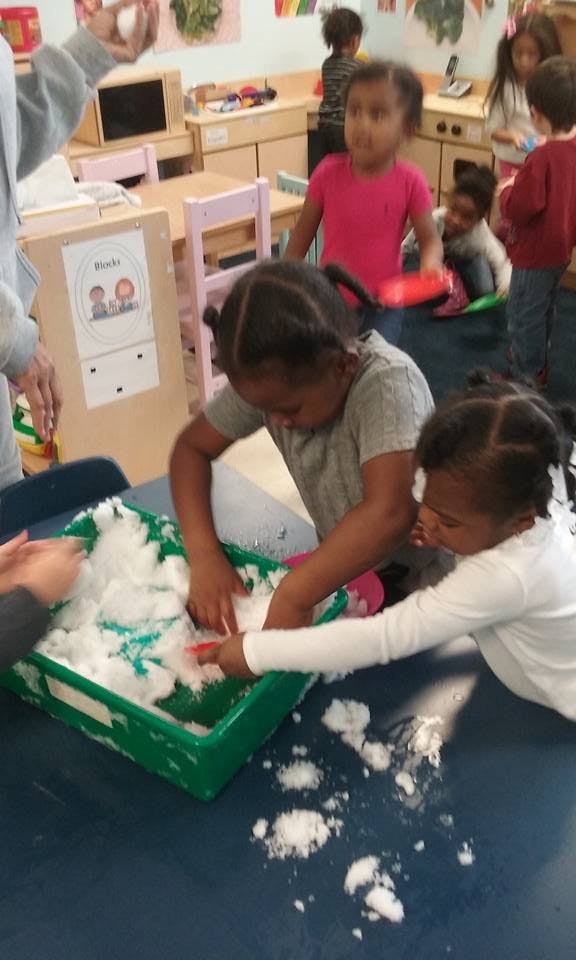 Two children playing with white material in a green bin