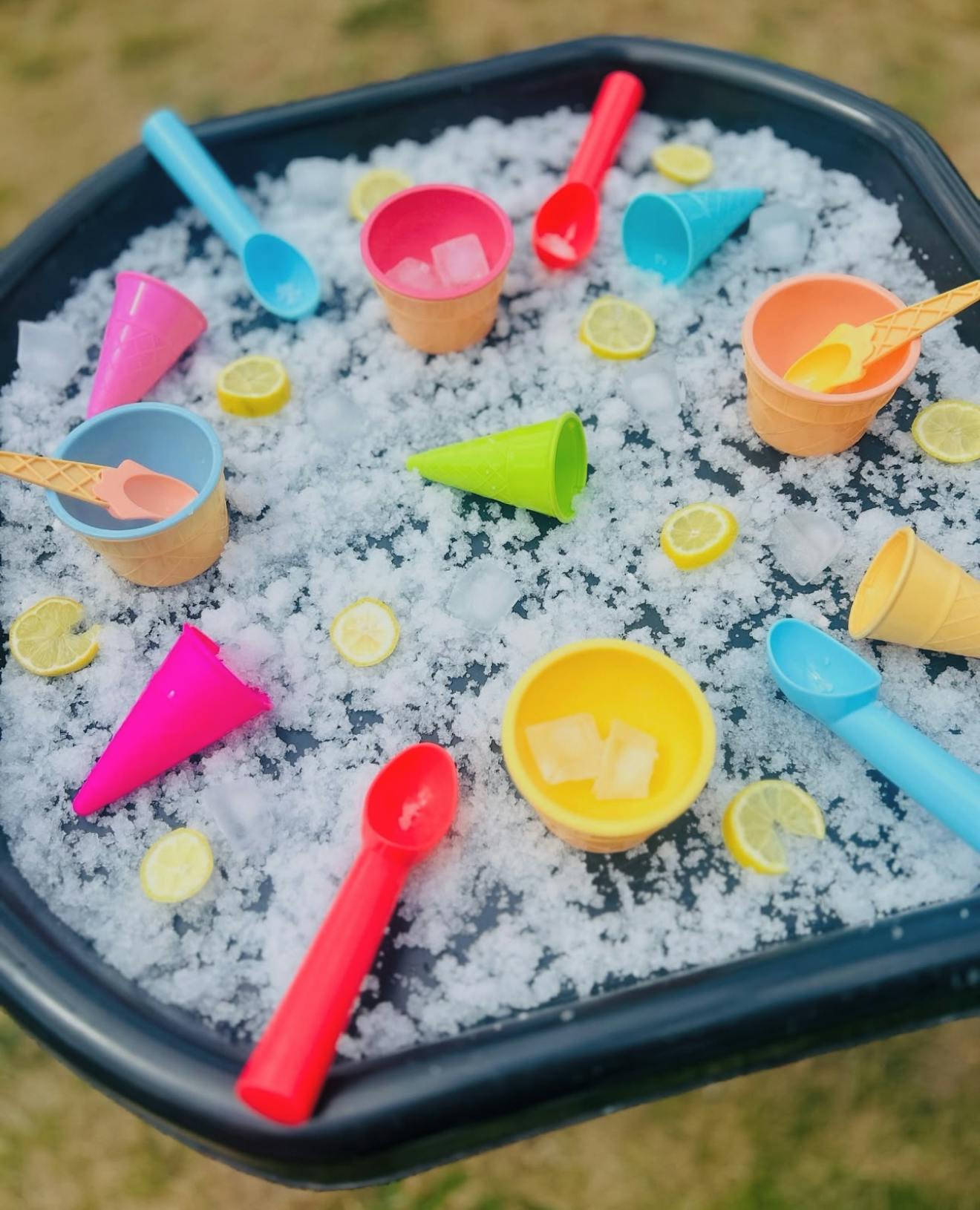 Play ice cream set with colorful scoops, cups, and cones in crushed ice with lemon slices