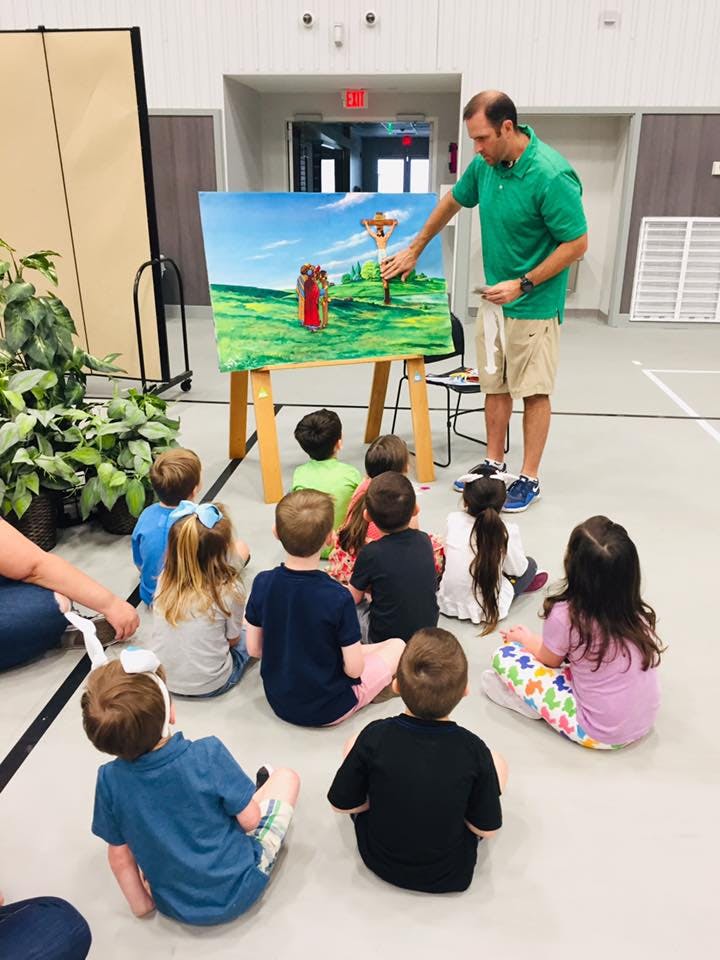 Adult teaching children with a painting on an easel