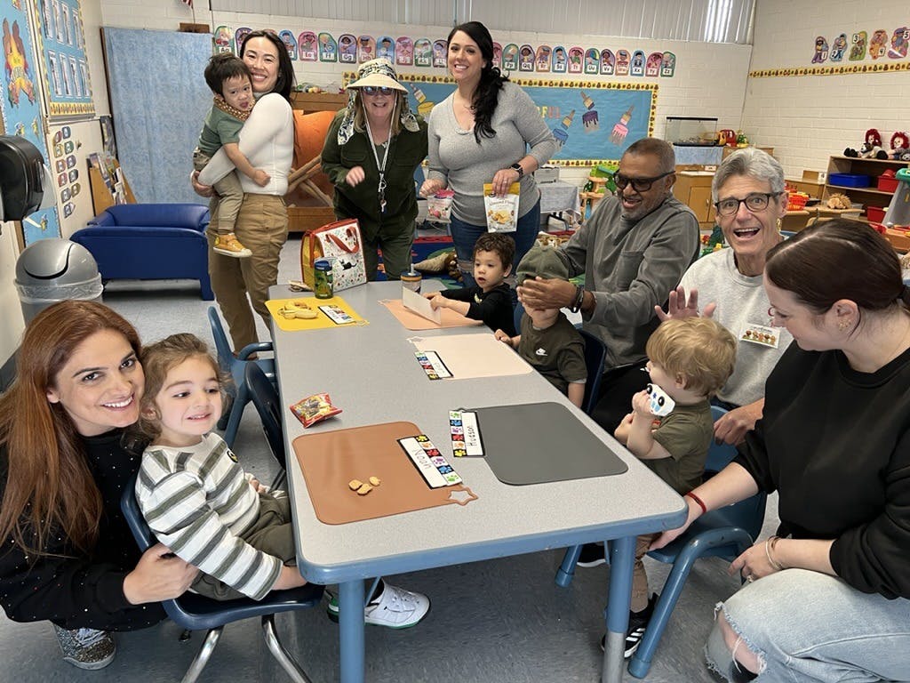 Adults and children gathered around tables in a classroom