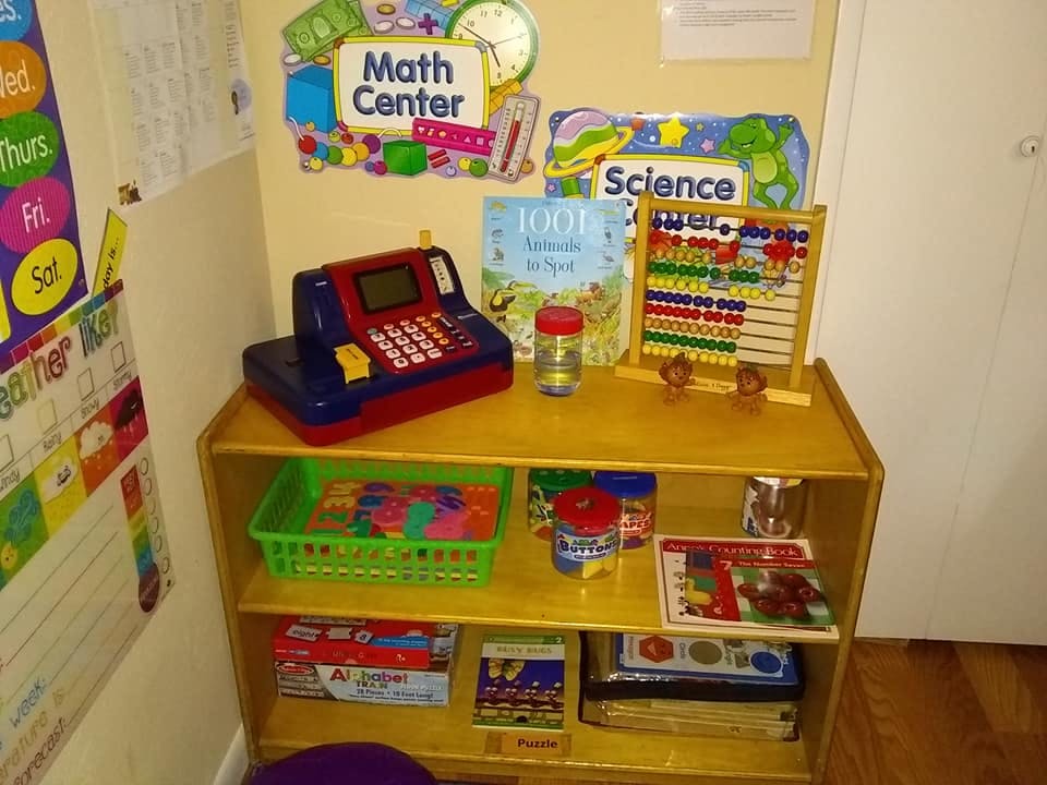 Play cash register, abacus, and books on a wooden shelf in a classroom