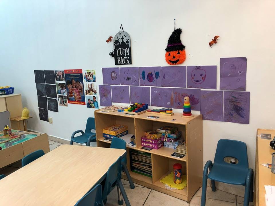 Classroom with tables, chairs, shelves, and children's artwork on the wall