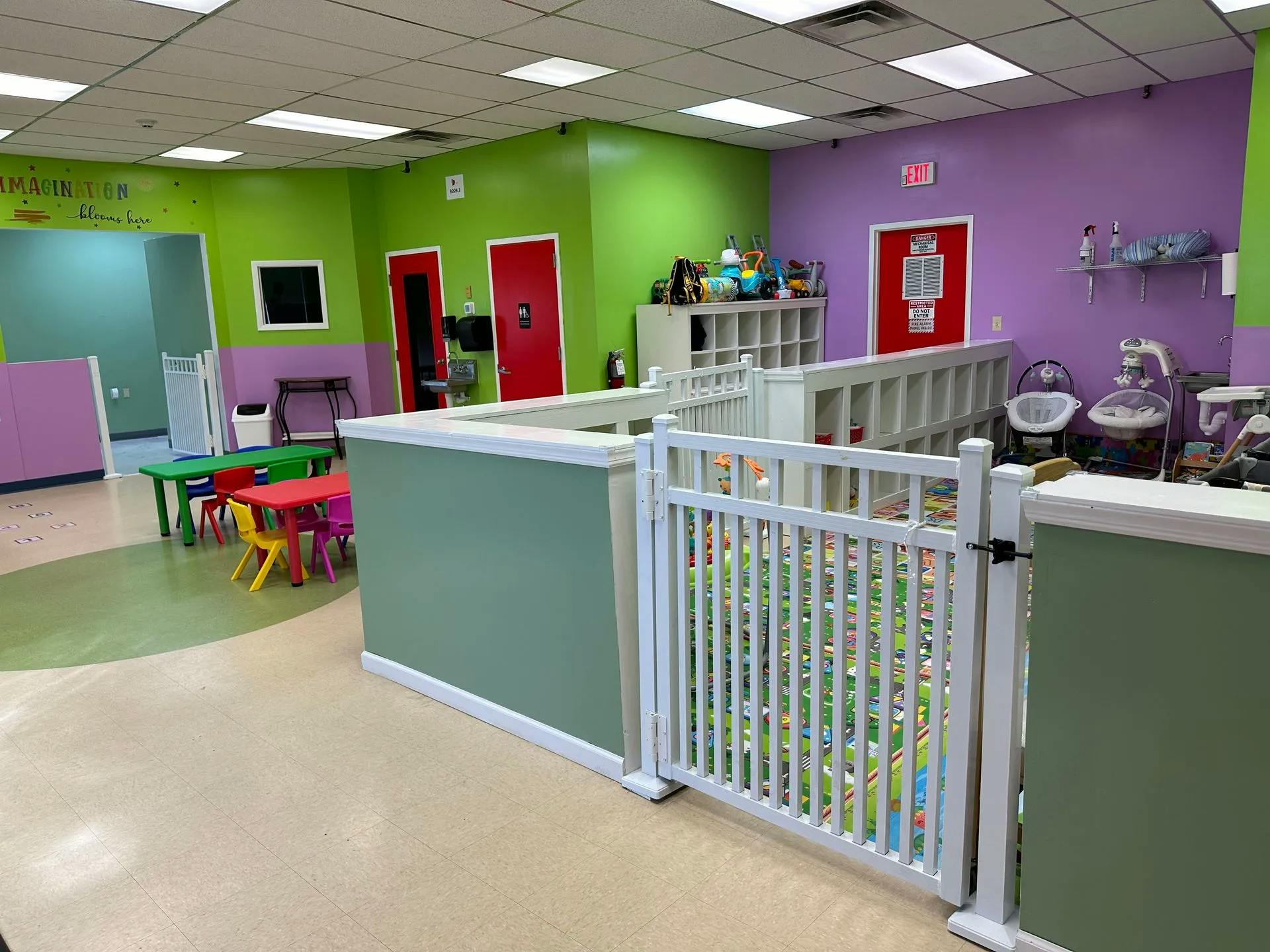 Indoor play area with colorful walls, small tables, and a white safety gate