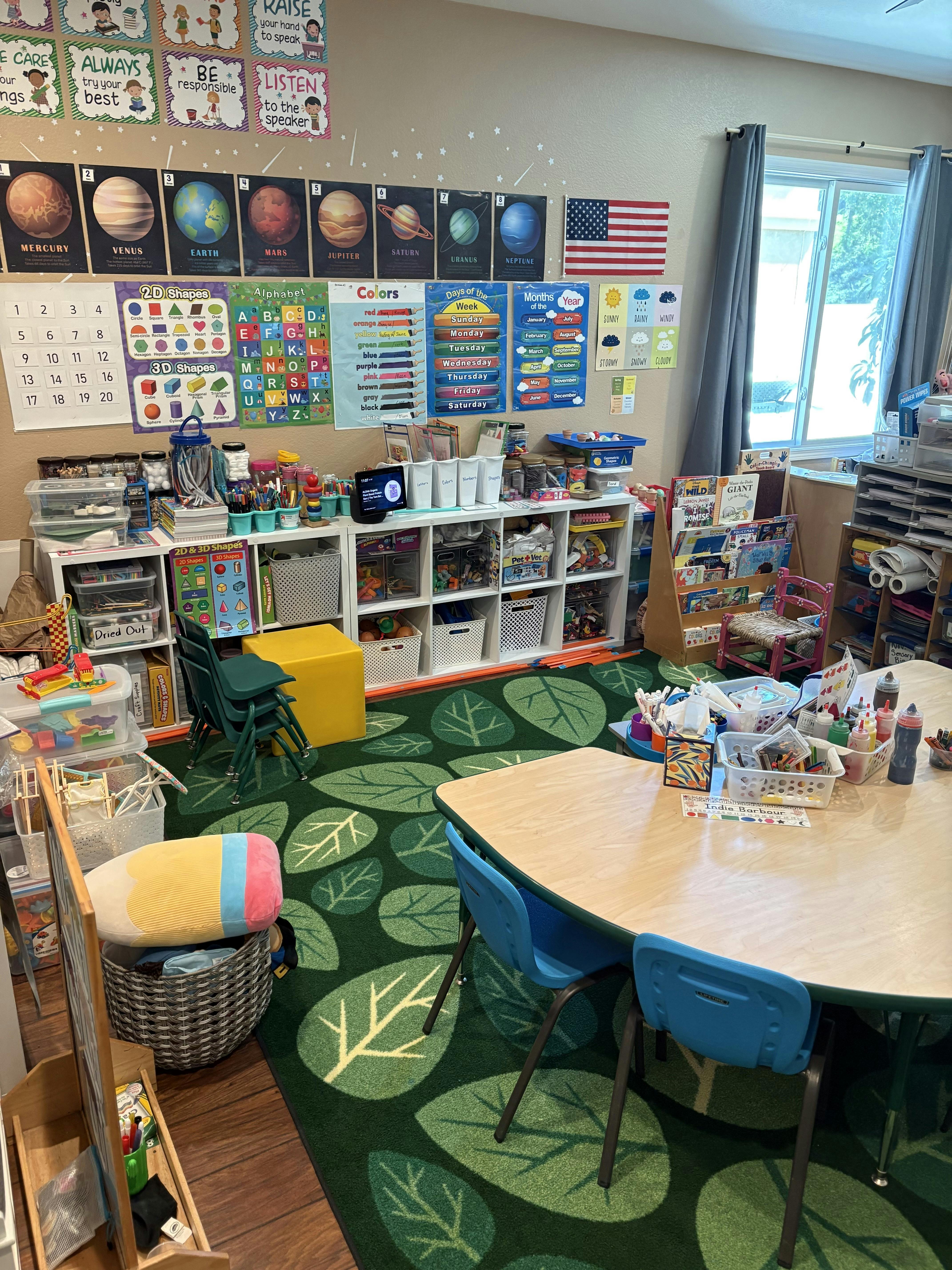Classroom with educational posters, shelves of supplies, and small tables with chairs