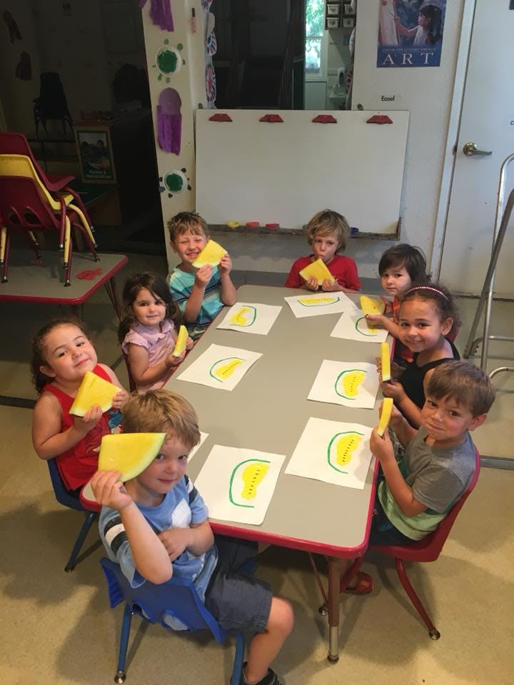 Children sitting at a table with drawings and yellow paper cutouts
