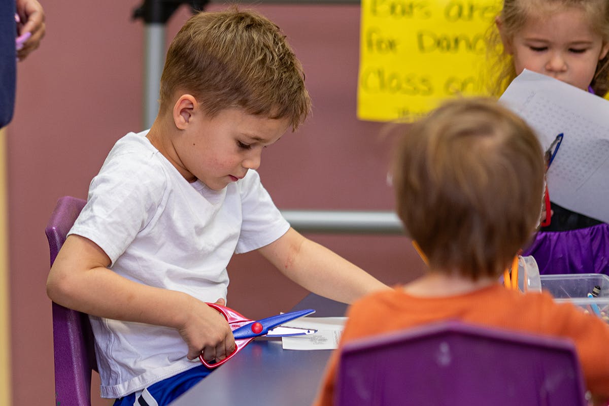 Child cutting paper with scissors at a table in a classroom
