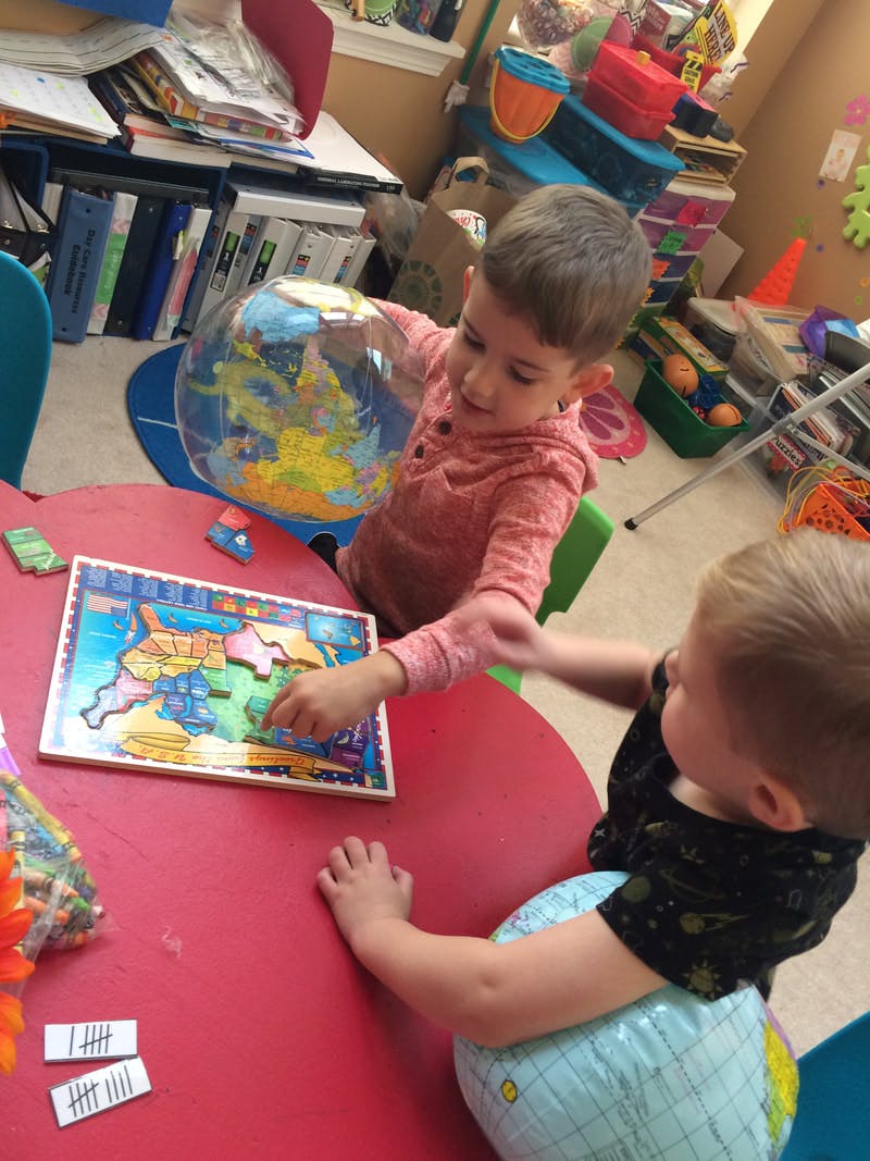 Two children playing with a puzzle and a globe at a red table