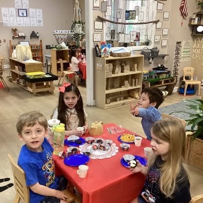 Four children sitting around a table with snacks and drinks in a classroom