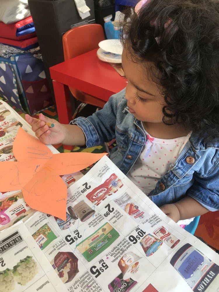 Child drawing on orange paper over a newspaper