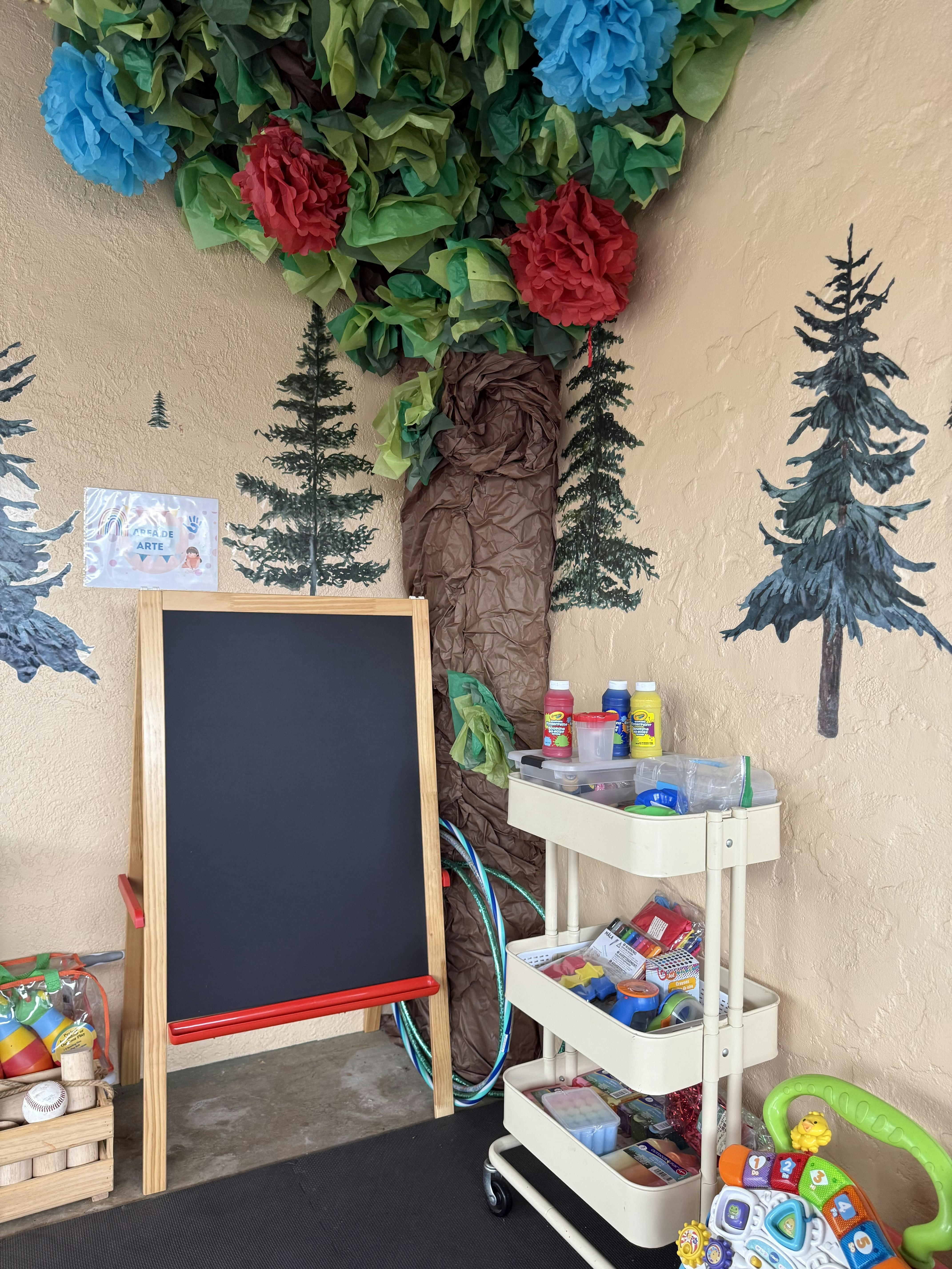 Easel with a blackboard, art supplies on a cart, and a tree mural on the wall