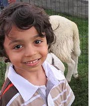 Child smiling with a sheep in the background