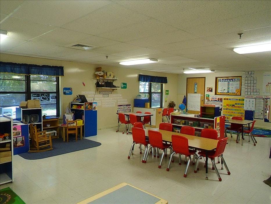 An empty classroom with small tables and red chairs