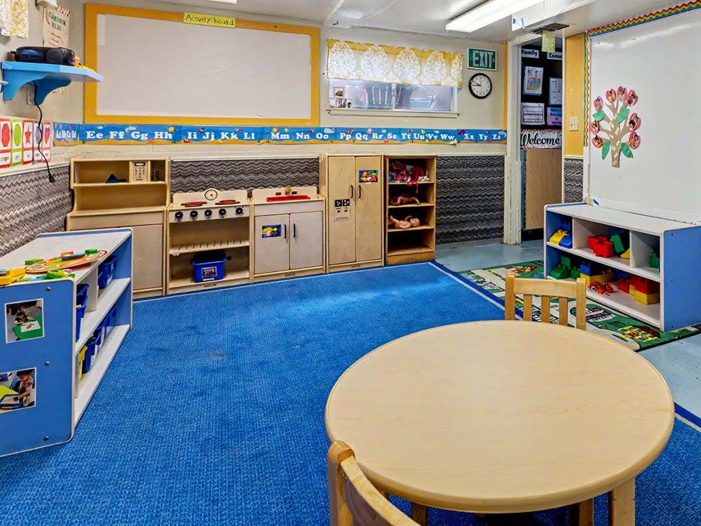 Empty classroom with activity board, play kitchen, and round table