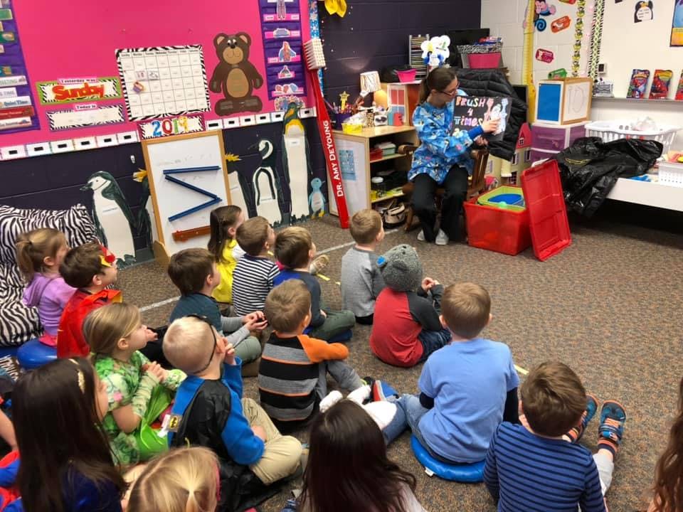 Adult reading to a group of children sitting on the floor in a classroom