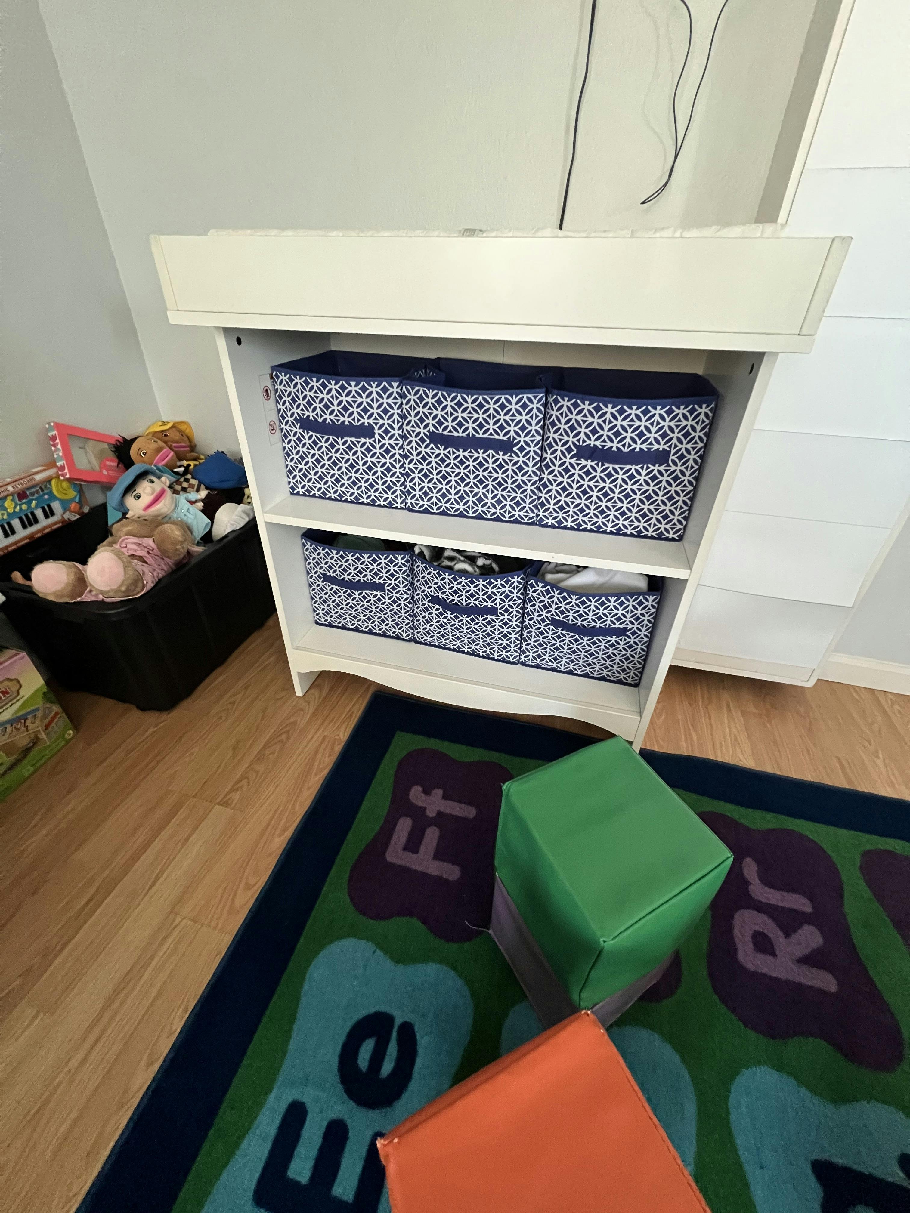 White changing table with navy blue patterned storage bins in a child's room