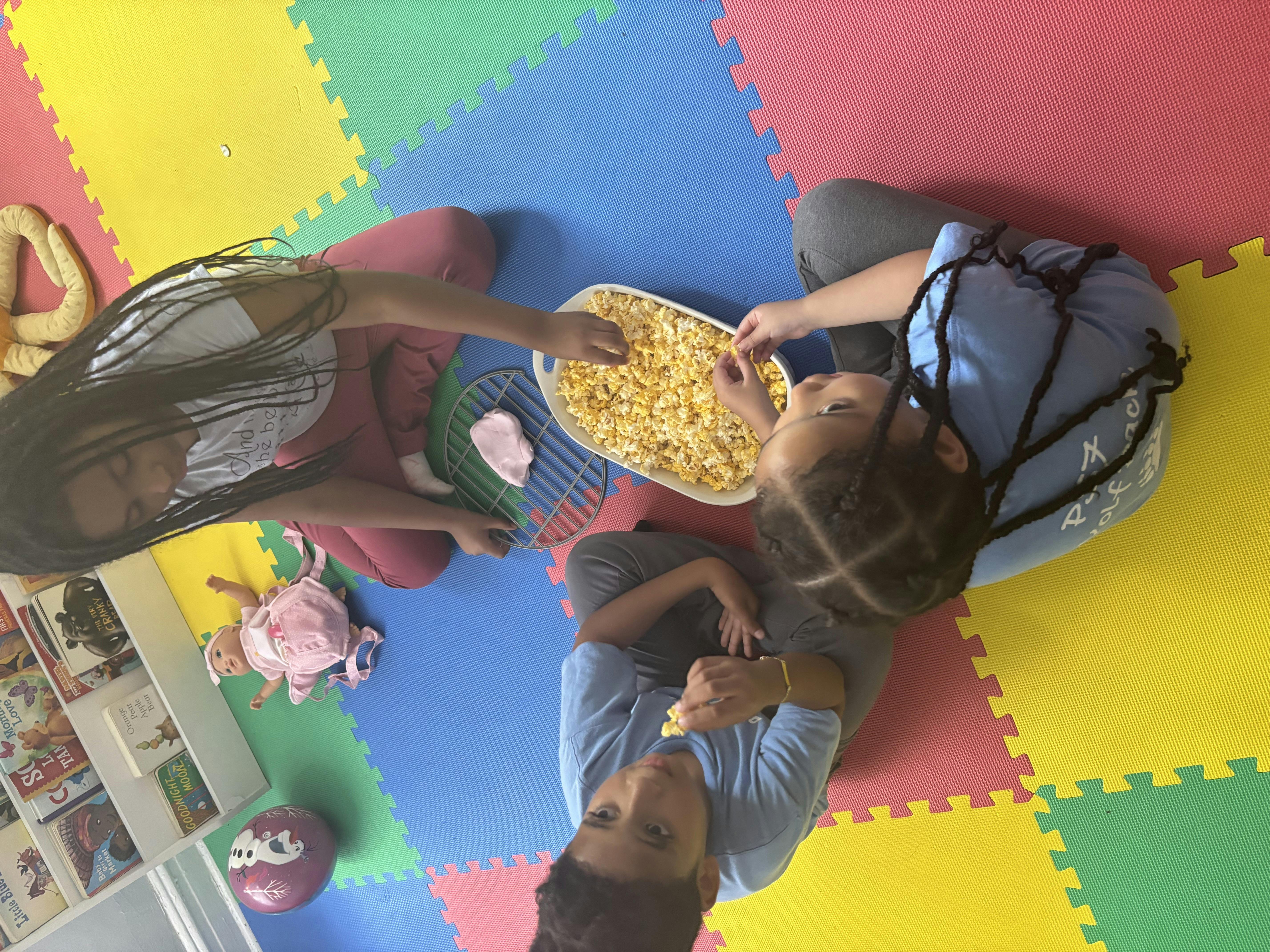 Two children sharing popcorn on a colorful mat