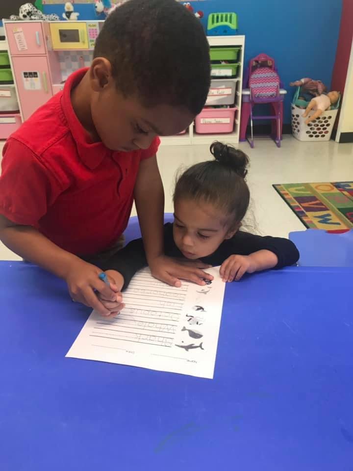 Two children looking at a paper on a blue table in a classroom