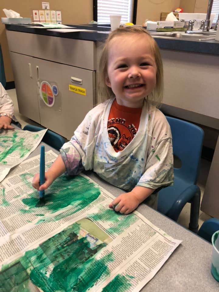 Child painting green on newspaper at a table